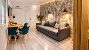Una sala de estar moderna con un sofá gris, sillas color turquesa, una mesa de comedor de madera y un papel tapiz estampado.