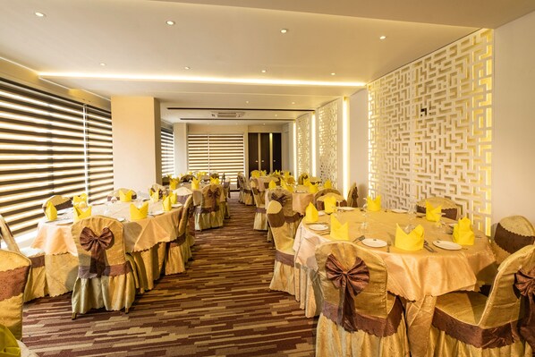 Un salón de banquetes con mesas redondas, sillas adornadas con lazos y una pared con diseño.