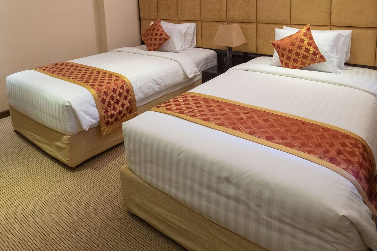 A hotel room with two beds, a nightstand, a lamp, and a painting on the wall.