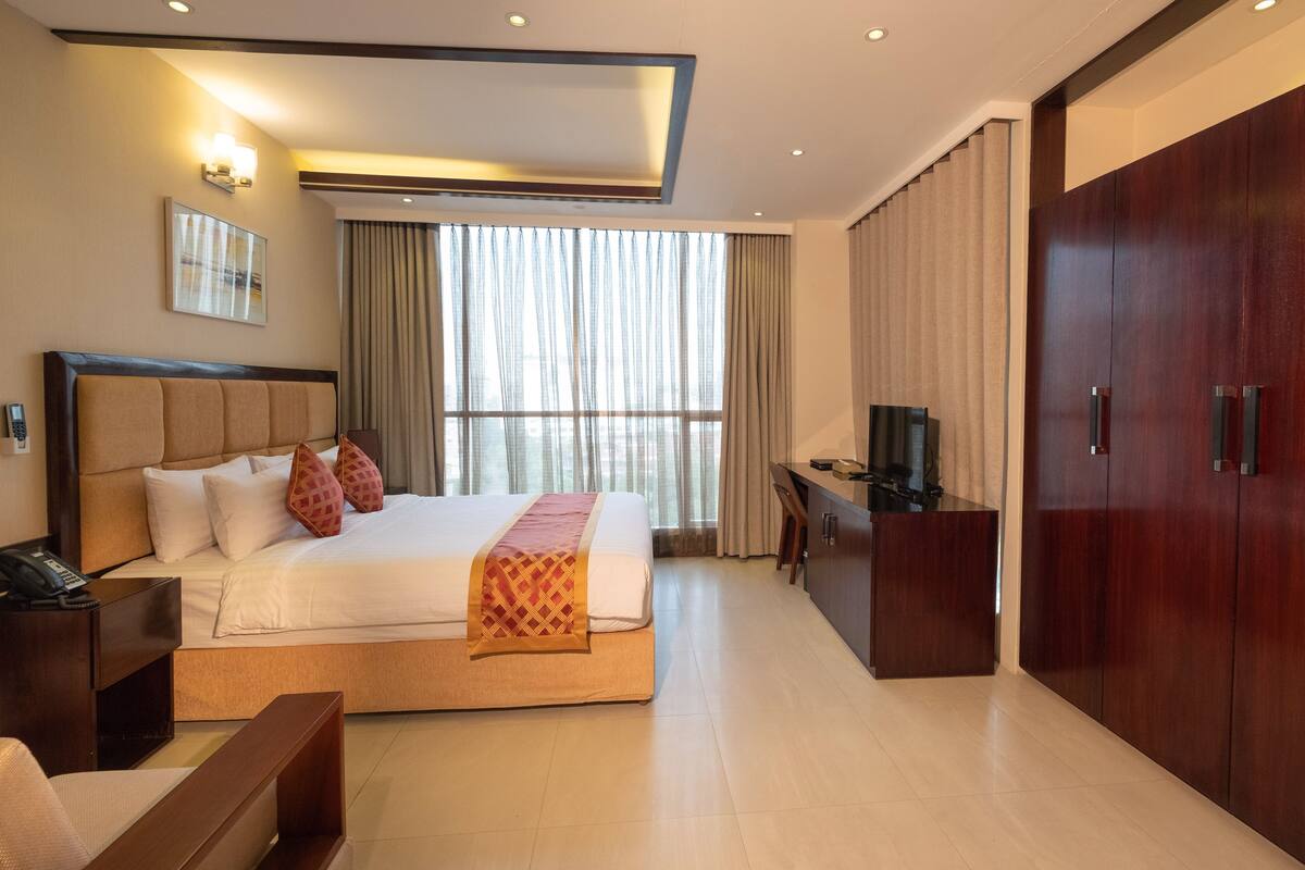 A hotel room with a large bed, a desk, a wardrobe, and a TV.