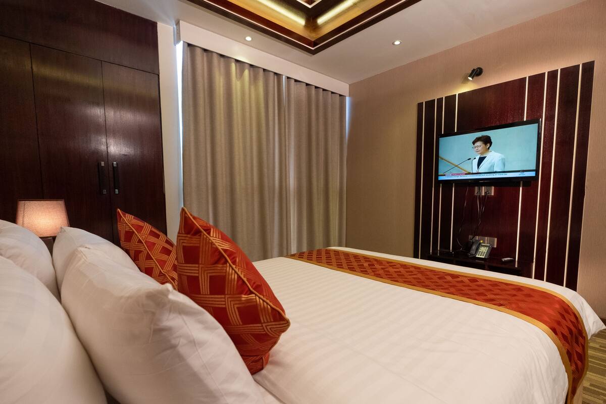 A hotel room with a large bed, a television mounted on the wall, and a window with curtains.