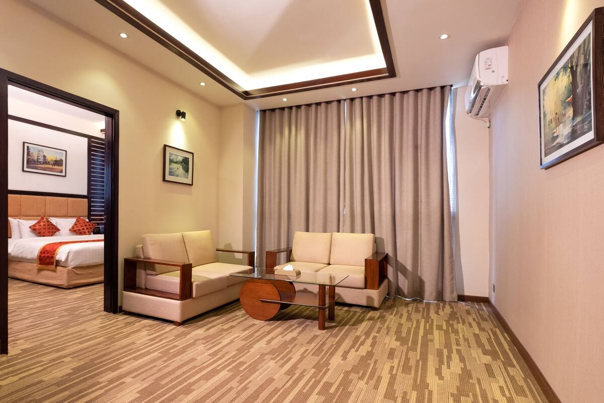 A hotel room with a bed, two sofas, a coffee table, and a painting on the wall.