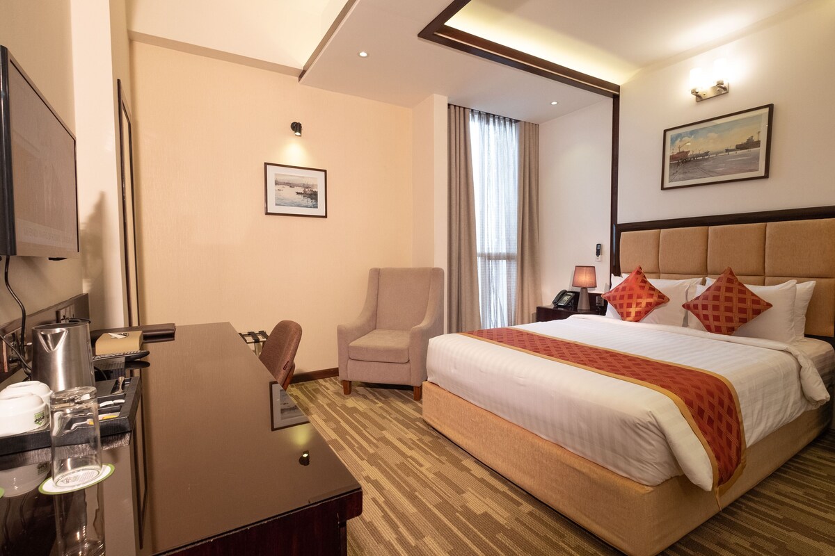 Una habitación de hotel con cama, escritorio, silla, televisor y ventana con cortinas.