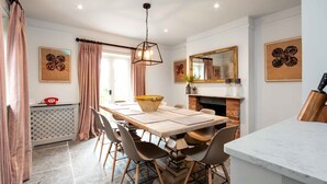 Een eetruimte met een grote houten tafel, stoelen, een hanglamp en een open haard.