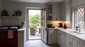 Een keuken met witte kasten, een fornuis en een eethoek met rieten stoelen.