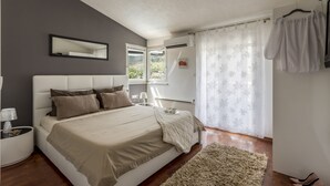 Un dormitori amb un llit gran, una tauleta de nit, un mirall i una finestra amb cortines.