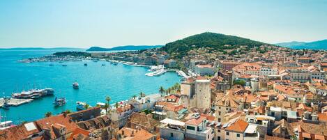 A coastal town with historic buildings, a harbor with boats, and a hill in the background.