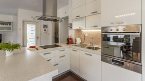 Una cuina moderna amb armaris blancs, una campana d'extracció d'acer inoxidable i un forn Bosch.