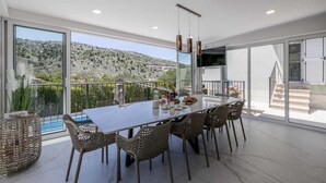 Una zona de menjador moderna amb una taula gran, cadires de vimetlla i vista a un paisatge de muntanyes.
