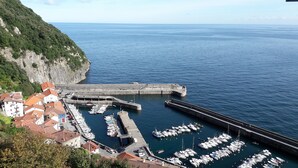 A coastal marina with boats docked, a stone pier, and buildings with red-tiled roofs. - Bekozu Apartment, Urresti (Gautegiz Arteaga)