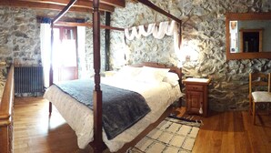 A four-poster bed in a stone-walled room with a wooden floor, a small bedside table, and a chair. - Bekozu Apartment, Urresti (Gautegiz Arteaga)
