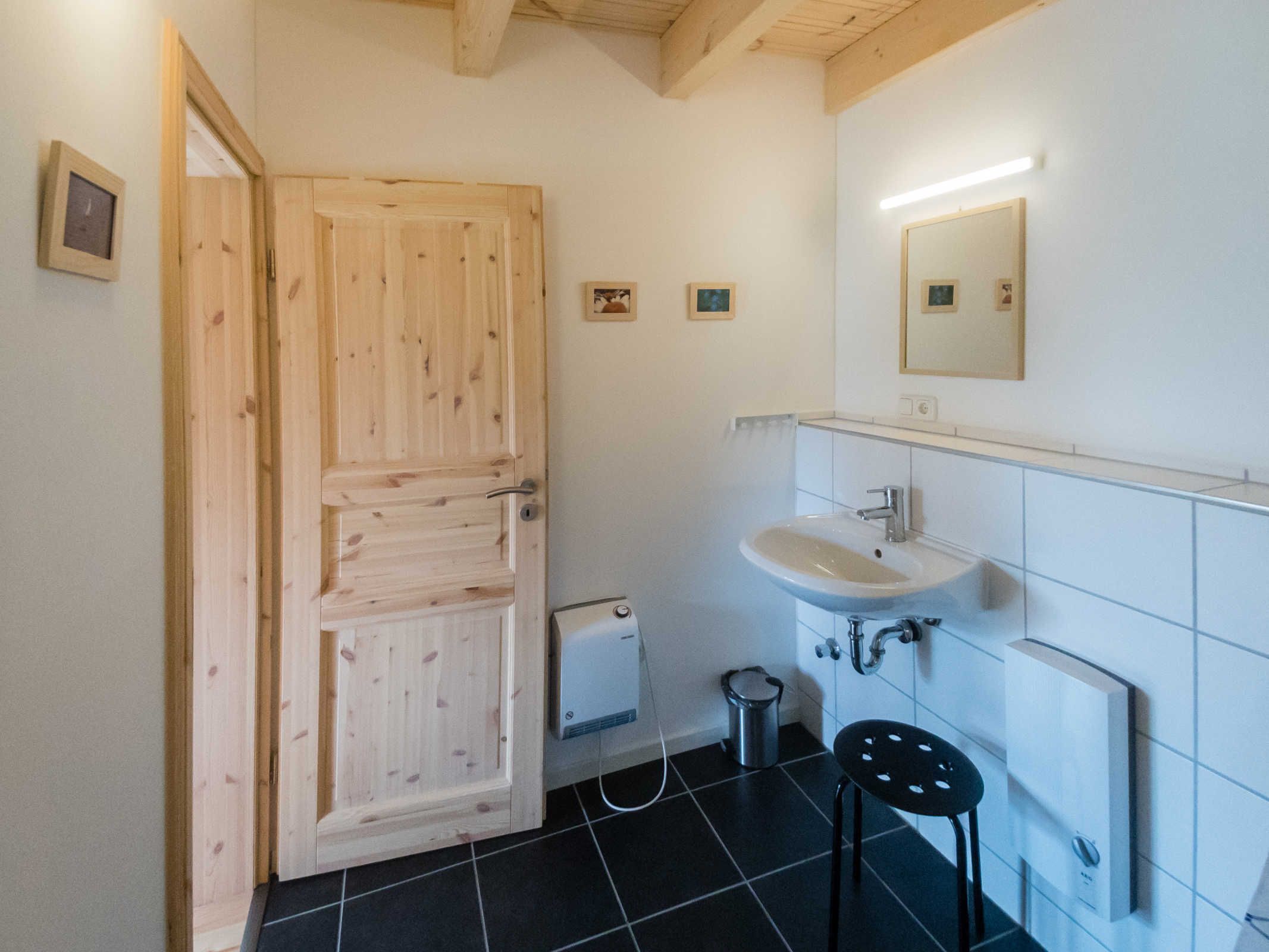 A bathroom with a wooden door, a white sink, a mirror, and a black stool.