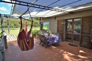 A covered patio area with a table set for dining, a hanging hammock, and a view of the garden. - Nice apartment with large Terrace.. (Capoliveri)