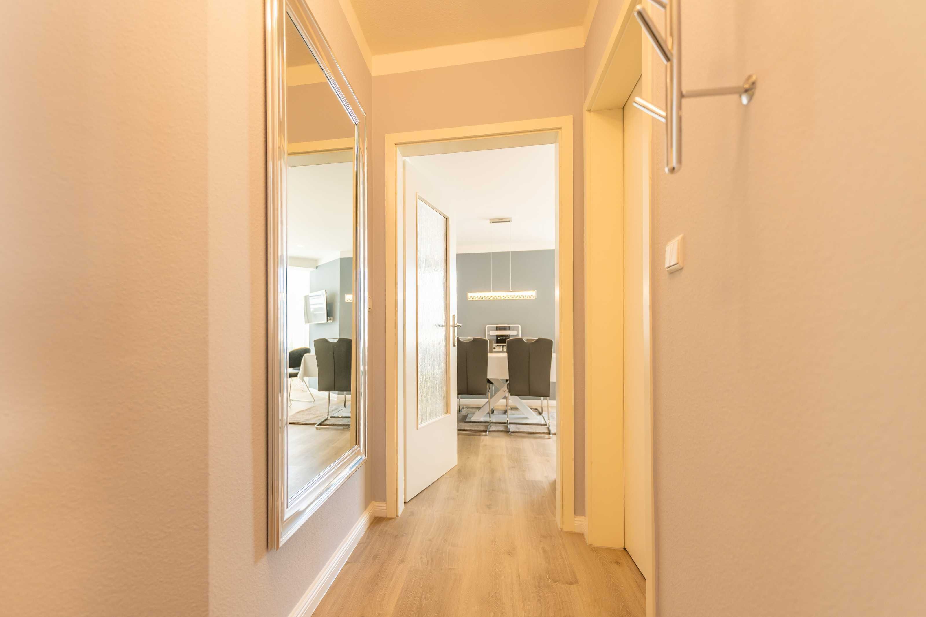 Een hal met een spiegelwand, die leidt naar een kamer met een bureau en stoel.