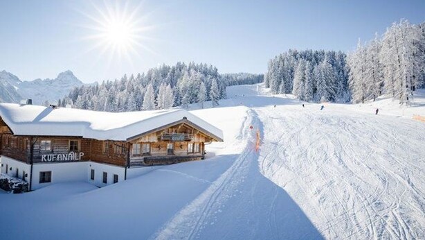 A snow-covered mountain landscape with a wooden building labeled 'RUFANALP' and a ski slope.
