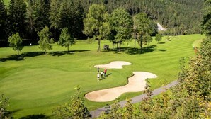 A golf course with a clear path, trees, and a mountainous backdrop.