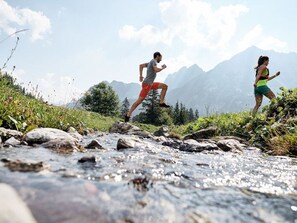 Dos personas corriendo a lo largo de un arroyo pedregoso, con montañas al fondo.
