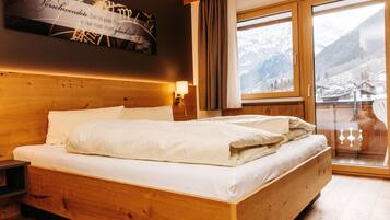 Un lit en bois dans une chambre avec vue sur les montagnes, visible à travers une grande fenêtre.