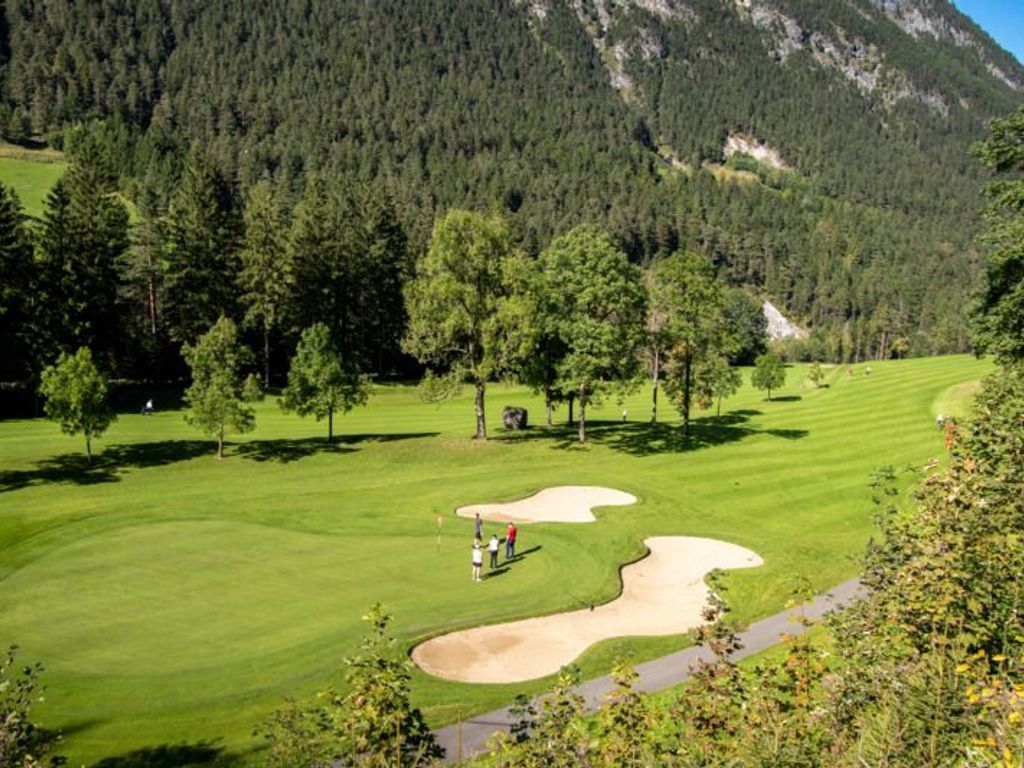 Un parcours de golf avec des allées bien définies, des arbres et une chaîne de montagnes en arrière-plan.
