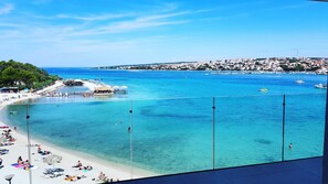 Blick auf die Küste mit Strand, klarem blauen Wasser und einer Stadt im Hintergrund.