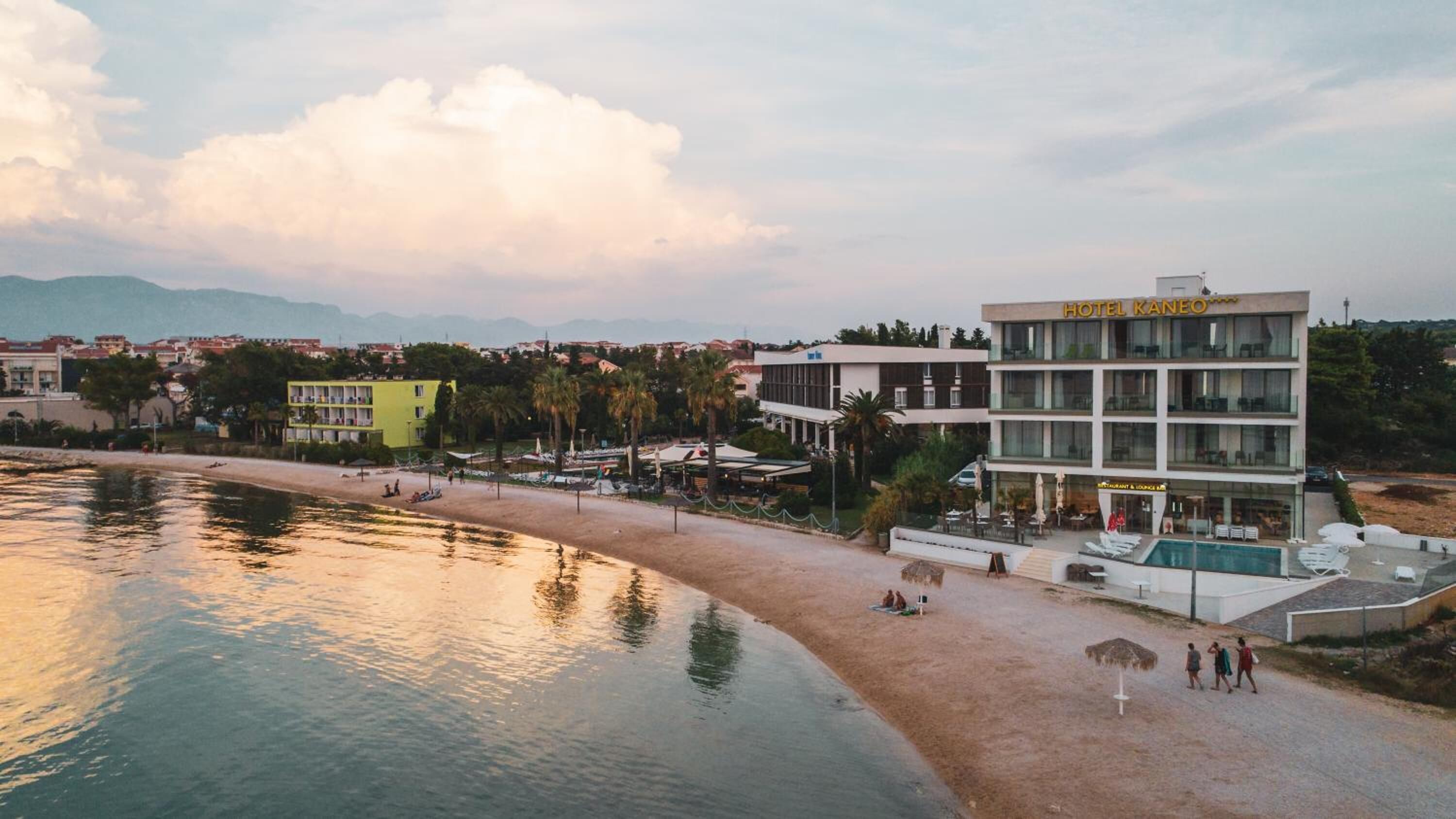 A hotel with a pool, beach, and mountain backdrop.