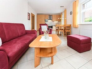 A modern living room with a red sofa, a wooden dining table, and a red ottoman. - Apartment Kegelrobbe - Haus an der Burg (Werdum)