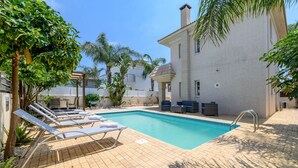 Une piscine avec des chaises longues, une terrasse en briques et un bâtiment doté d’un toit en tuiles.