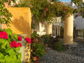 A courtyard with potted plants and flowers, stone walls, and a cobblestone path.
