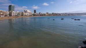 Eine Küstenstadt mit Strand, mehreren Booten und verschiedenen Gebäuden, darunter ein hoher, moderner Bau.