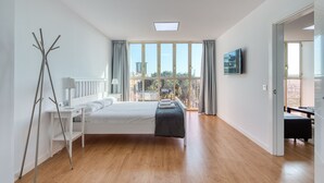 Ein modernes Schlafzimmer mit großem Fenster, einem Bett, einem Schreibtisch und einem Fernseher.
