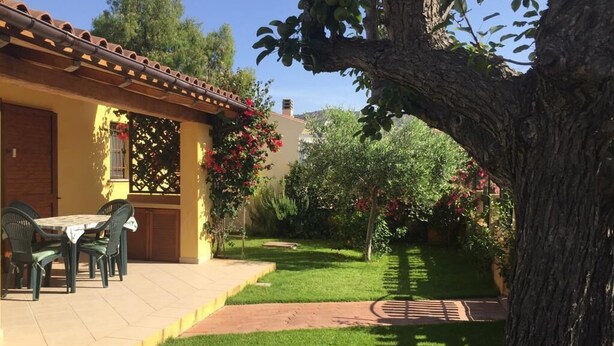 Eine Terrasse mit Tisch und Stühlen, ein kleiner Garten mit einem Baum und ein Gebäude mit einem Ziegeldach.