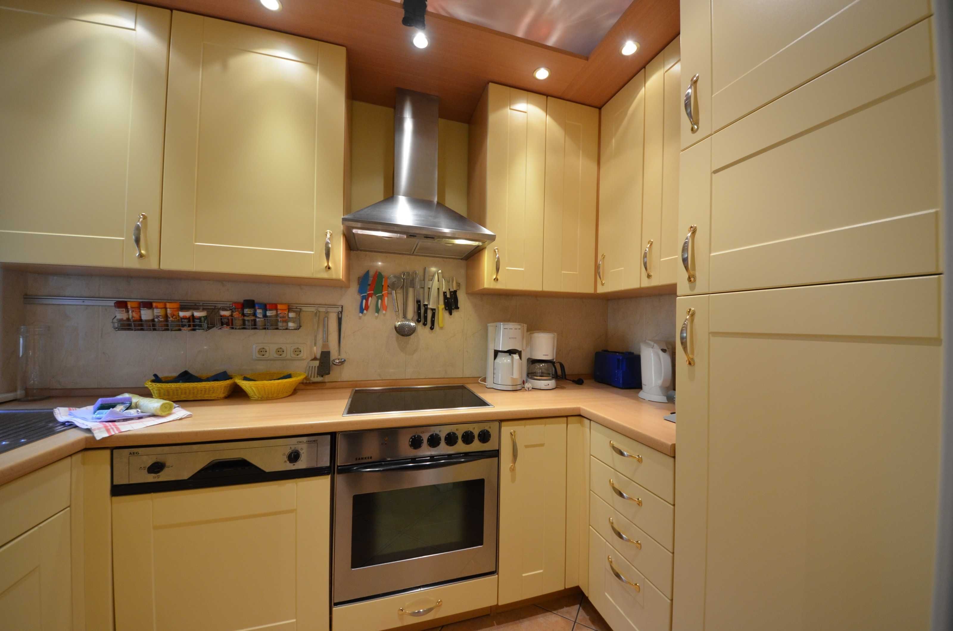 Una cocina con armarios color beige, una campana extractora de acero inoxidable, un fregadero, una estufa y una cafetera.