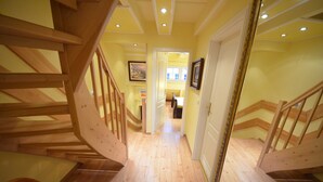 Una escalera de madera conduce a una habitación con piso de madera y una puerta con marco dorado.