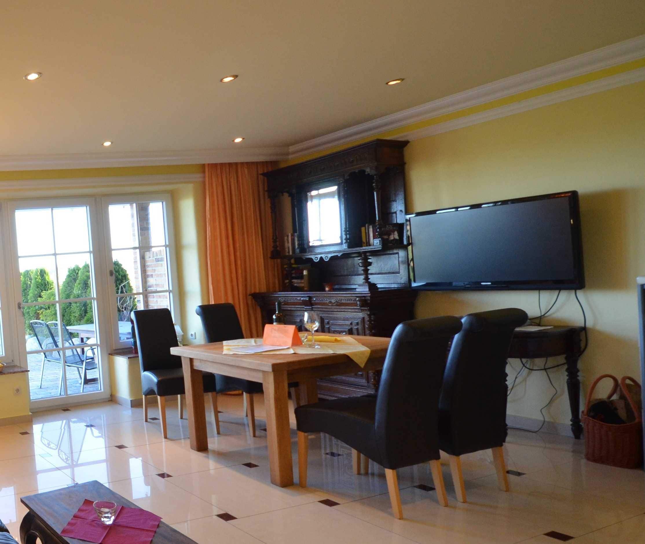 A dining area with a table, chairs, a television, and a view through the glass doors.