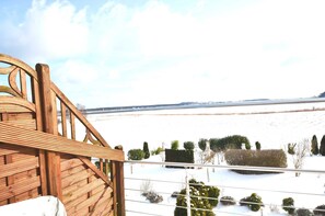 A wooden deck with a view of a snowy landscape and distant trees.