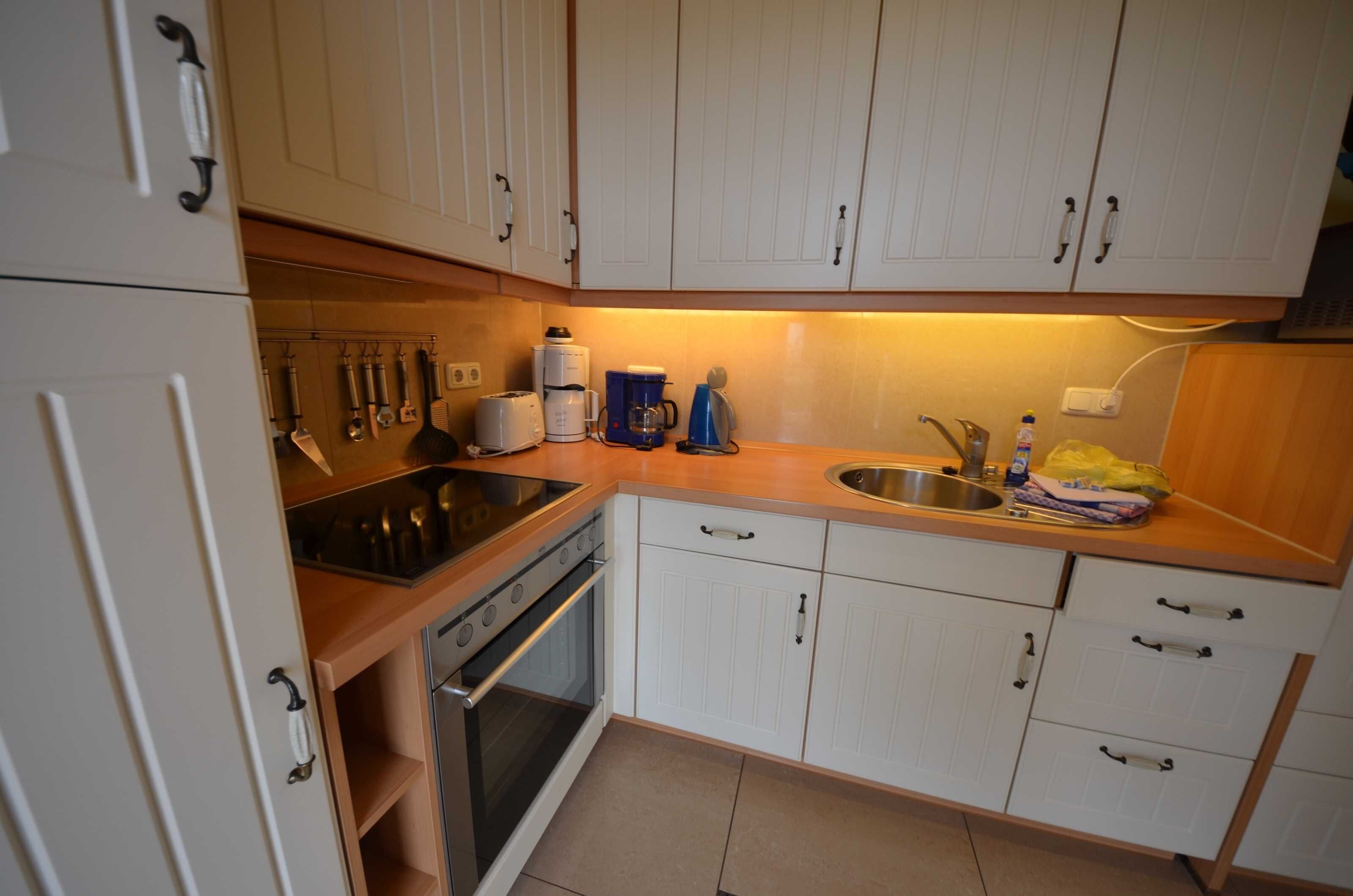 Een keuken met witte kastjes, een RVS spoelbak, een koffiezetapparaat en een broodrooster.