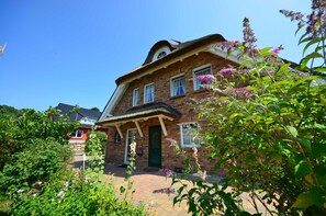 A brick house with a green door, a porch, and a garden with flowers. - 8a Reet-house part Sonnenkliff OG 3 bedrooms - Thatched-roof vacation apartments 8 Kröning (Gager)