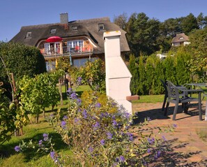 Ein Haus mit geneigtem Dach, einem Balkon mit einem roten Sonnenschirm und einem Garten mit violetten Blumen.