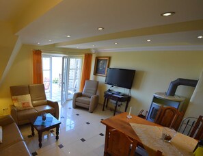 Una sala de estar con sofá, sillones, televisor, mesa de comedor y zona de cocina.