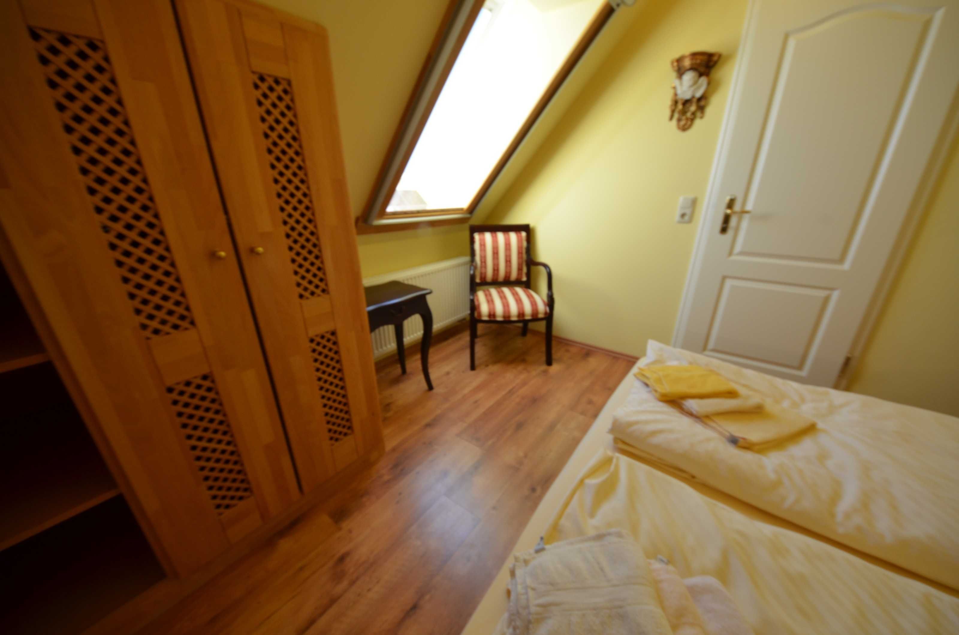 Une chambre avec un plafond en pente, une fenêtre, un lit, une chaise et une armoire.
