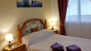 A neatly made bed with a quilted cover, a bedside lamp, a nightstand with a telephone, and a painting on the wall.