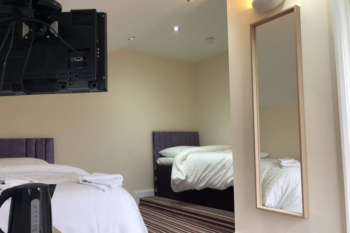 A hotel room with two beds, a large mirror, a television mounted on the wall, and a kettle on the table.