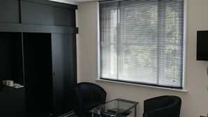 Een moderne slaapkamer met een zwarte garderobe, een glazen tafel, twee zwarte stoelen, een gestreept tapijt en een raam met jaloezieën.