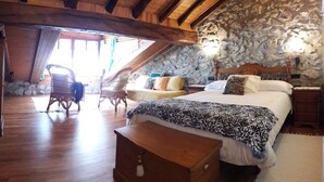 A cozy bedroom with a stone wall, wooden ceiling beams, a large bed with patterned bedding, two wicker chairs, and a bench. - Txoritoki Apartment, Urresti (Gautegiz Arteaga)