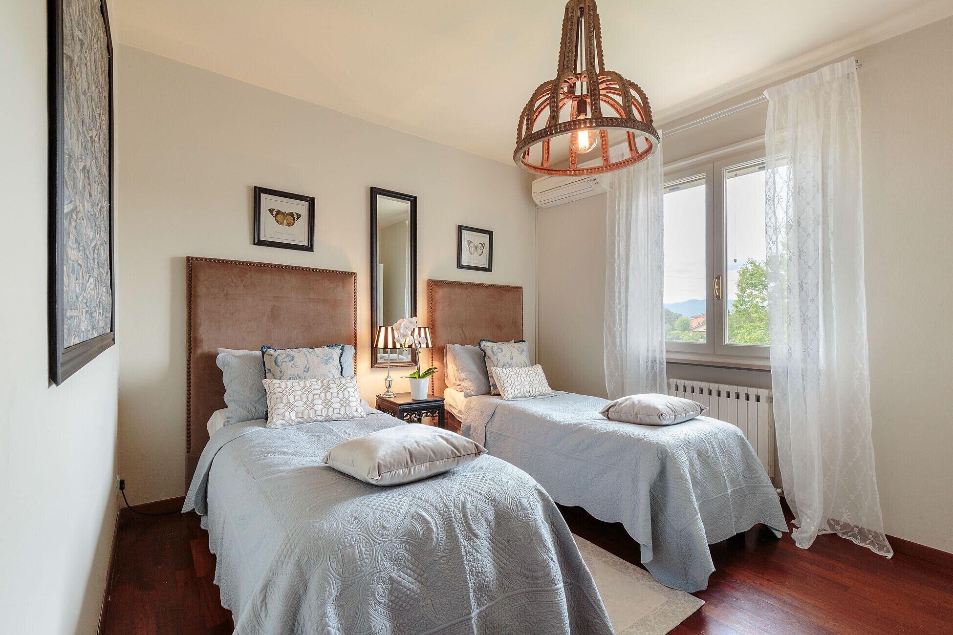 A bedroom with two beds, a large mirror, and a chandelier.