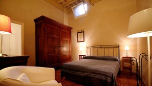 A bedroom with a wooden wardrobe, a bed with a grey bedspread, a chair, and two bedside lamps.
