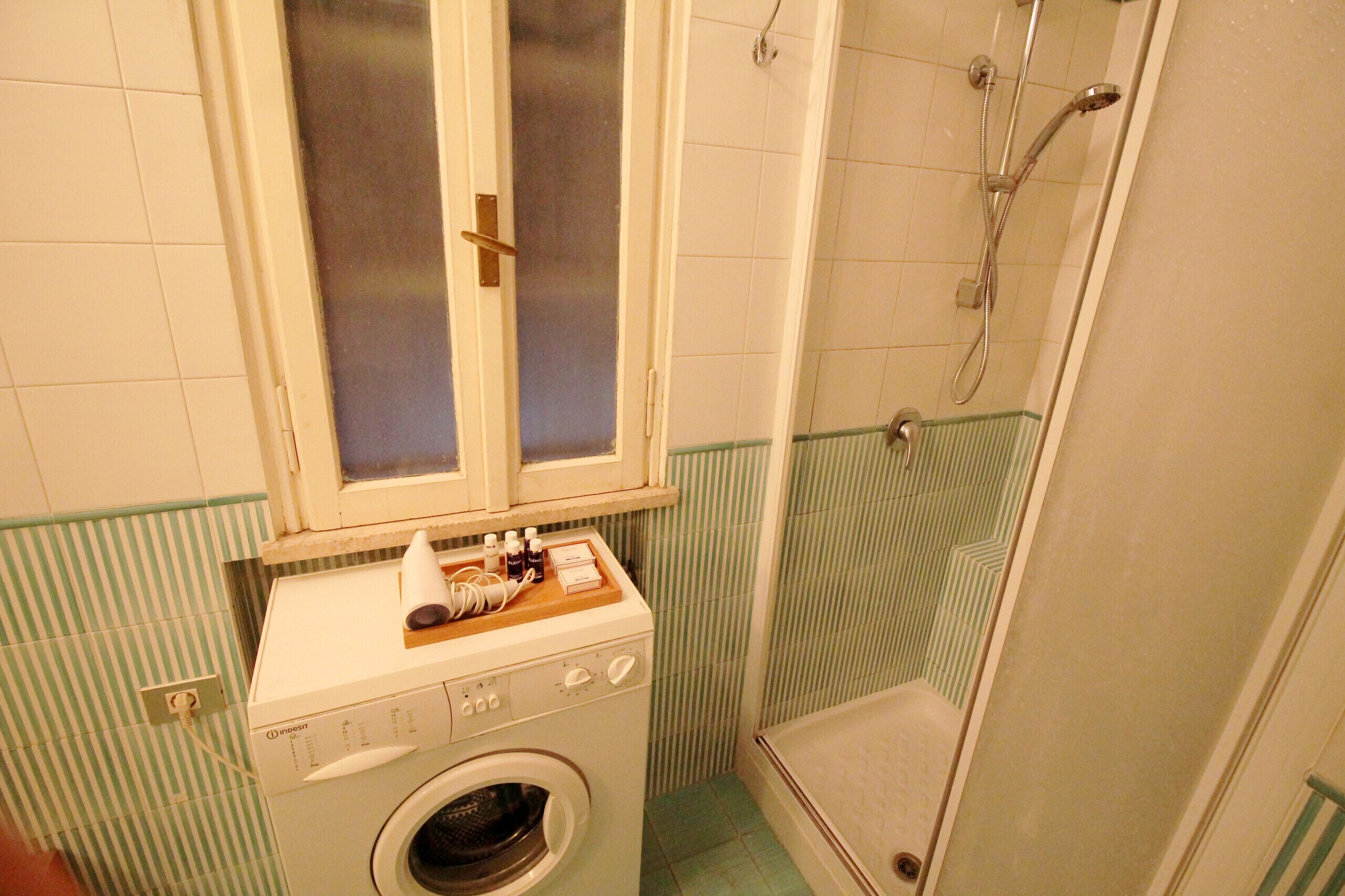 Ett litet badrum med tvättmaskin, dusch och toalett.