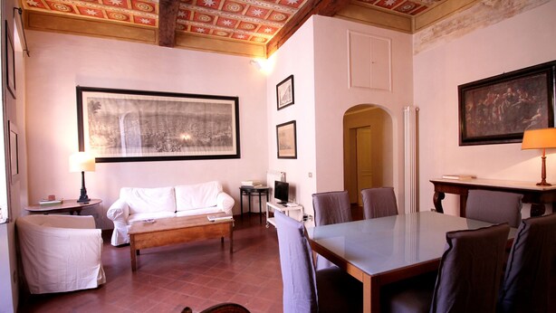 A room with a dining table, chairs, a sofa, a TV, and framed pictures on the walls.