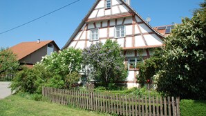 A traditional half-timbered house with a sloped roof, surrounded by lush greenery and a wooden fence. - An oasis for parents, a paradise for children (Tettnang)