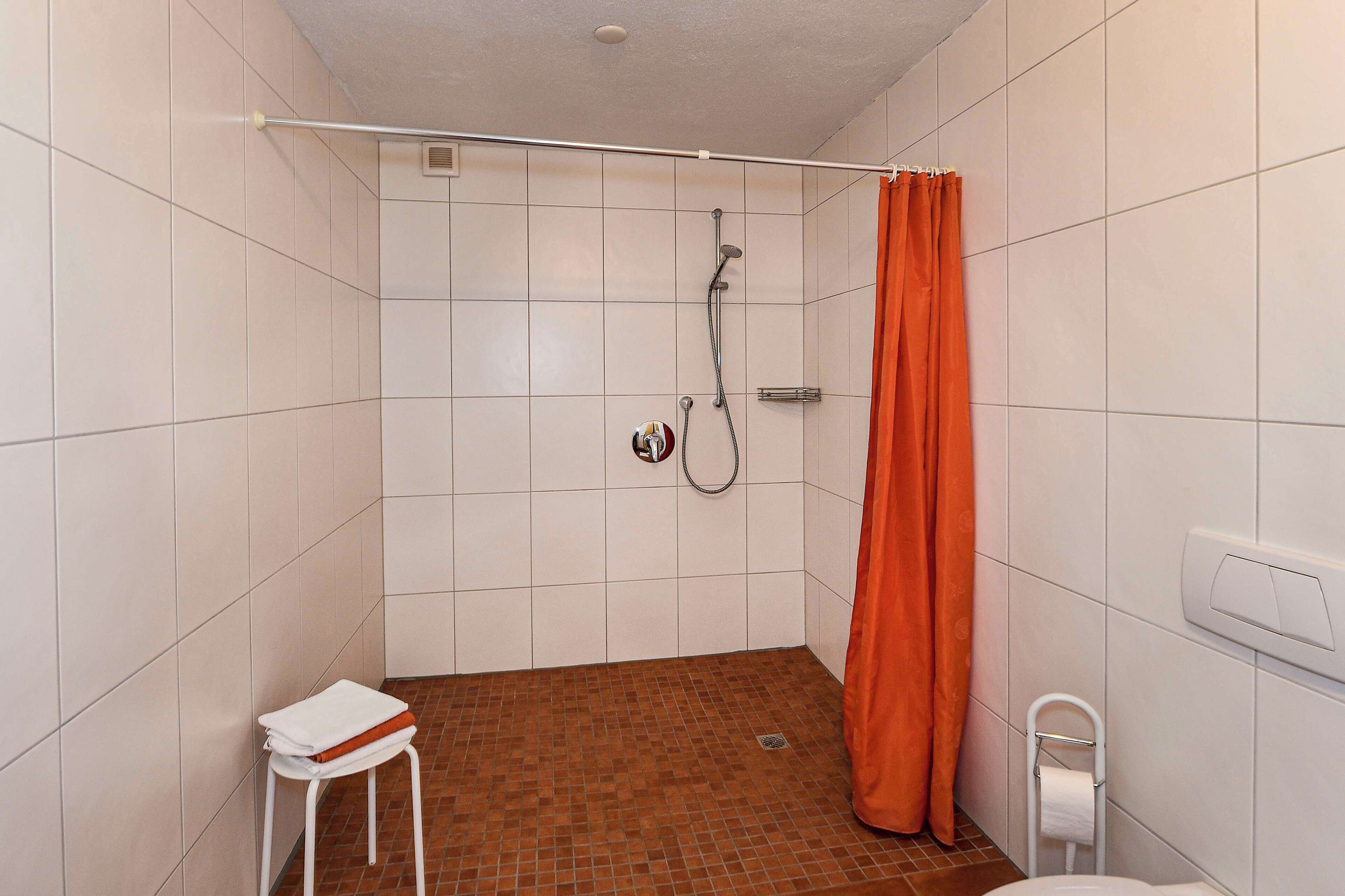 Une petite salle de bain avec une douche, des toilettes et un petit tabouret.